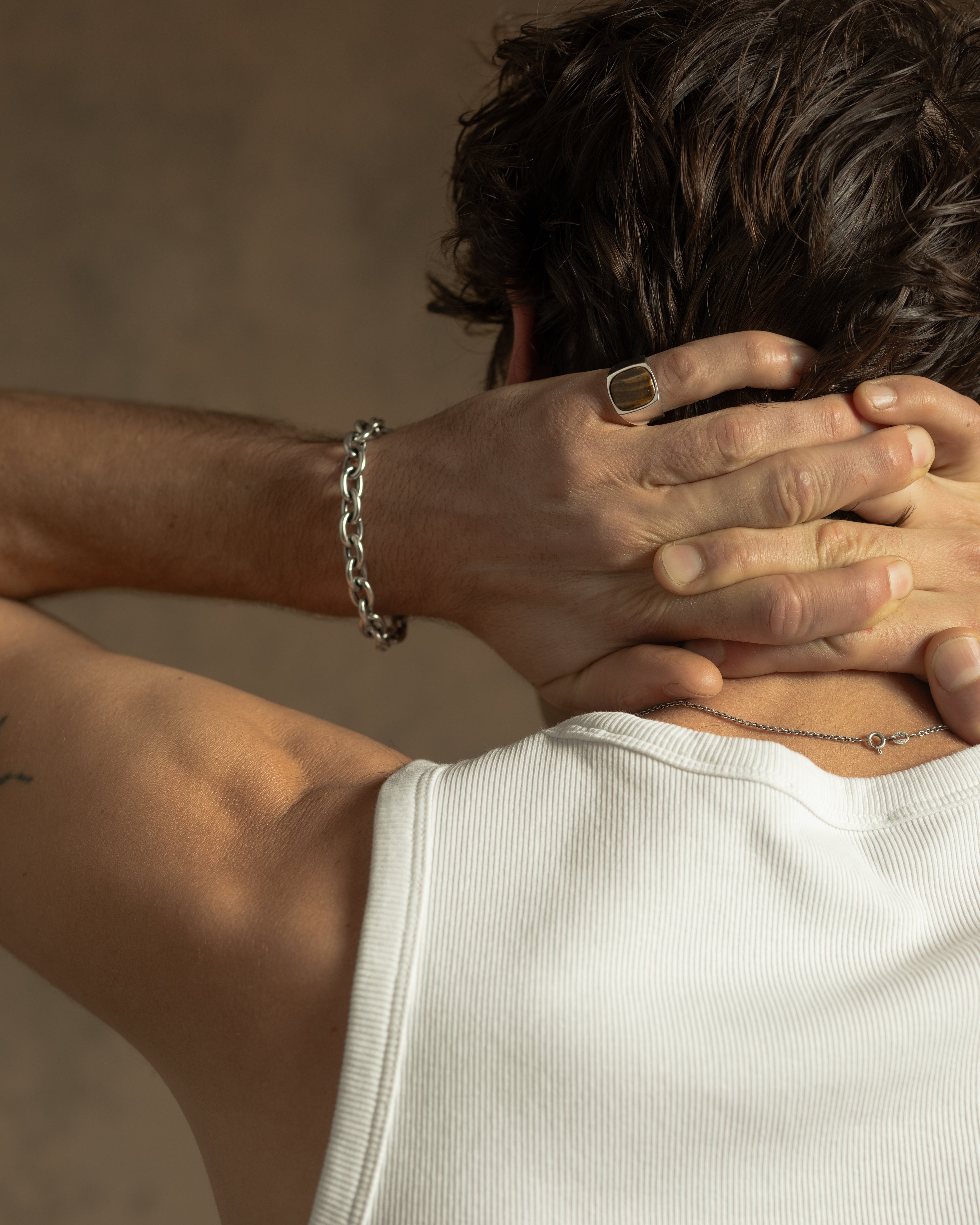 Close-up of a person wearing a silver bracelet and ring, with hands behind their head.