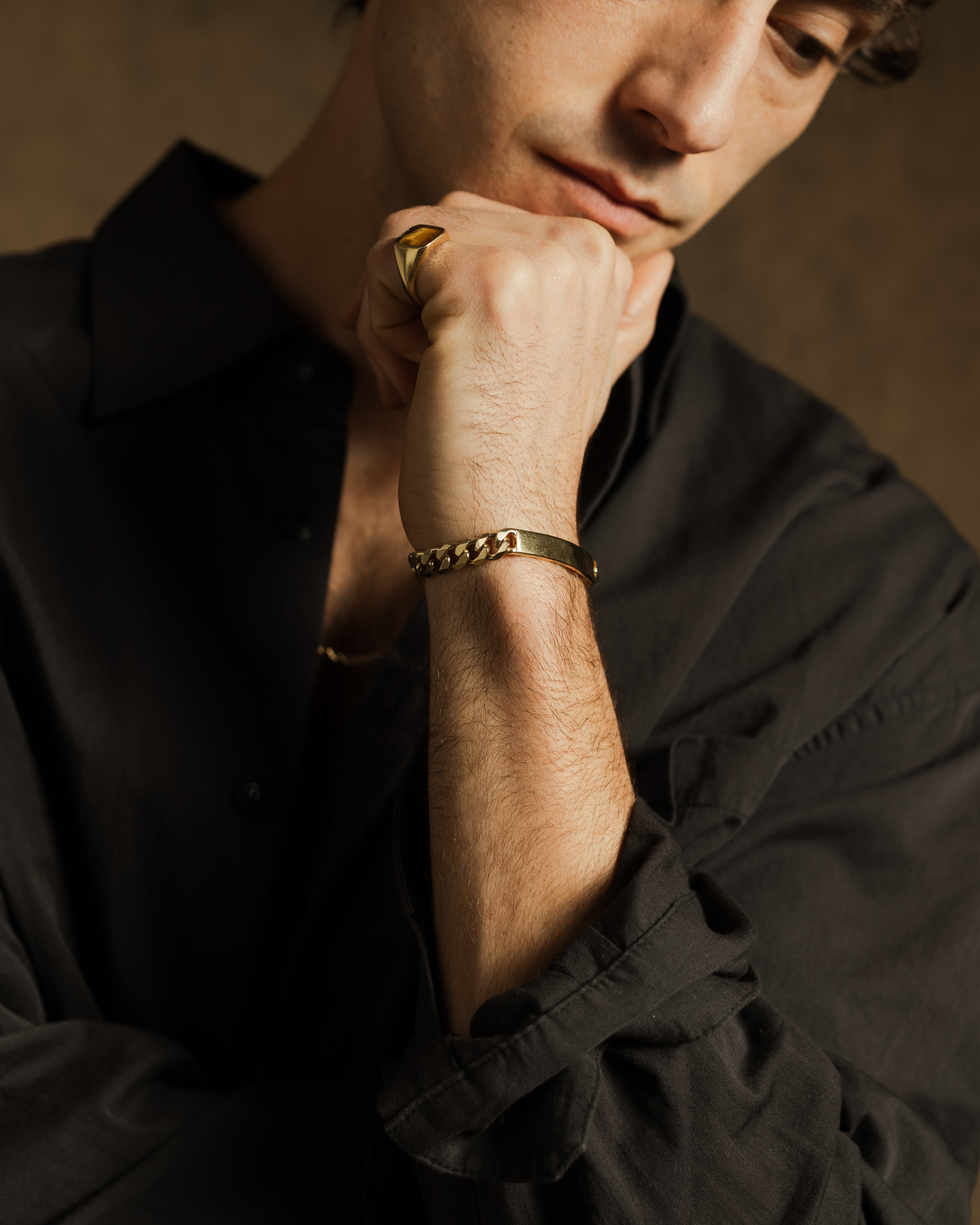 Man wearing a gold ring and bracelet, with a neutral background