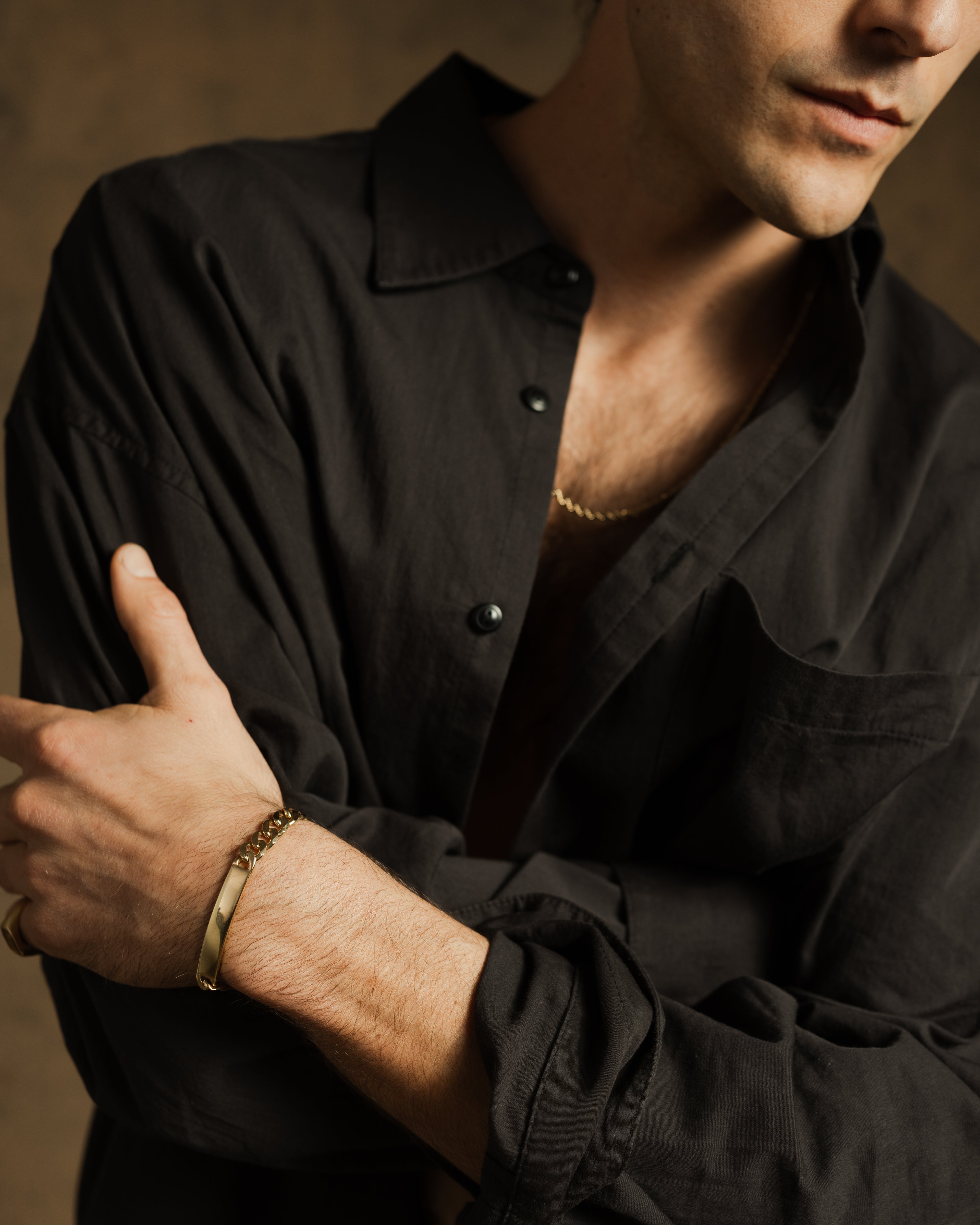 Man wearing a black shirt with a gold bracelet on a neutral background